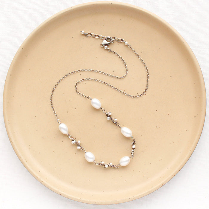 The oxidized silver pearl bud vine necklace styled on a tan plate to show the adjustable lobster clasp closure