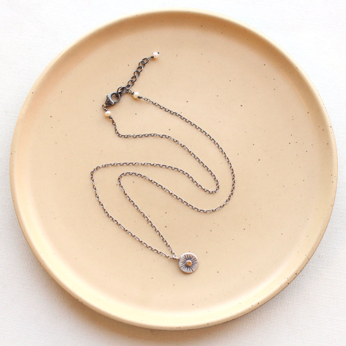 The rustic sun necklace styled on a tan plate to show the adjustable lobster clasp closure
