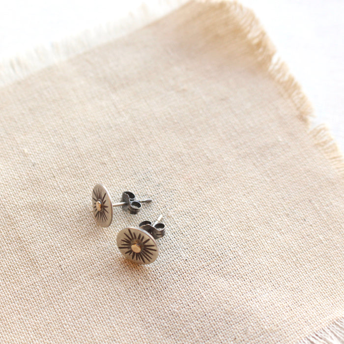 The rustic sun post earrings styled on tan linen to show the butterfly earbacks