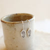 The rustic stamped silver feather lobe huggers styled on a ceramic cup