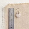 A silver raw silk disc earring next to a ruler for size reference