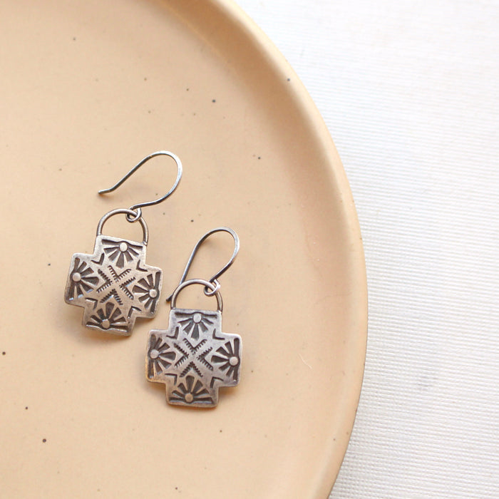 The southwest stamped silver sun cross earrings styled on a tan plate