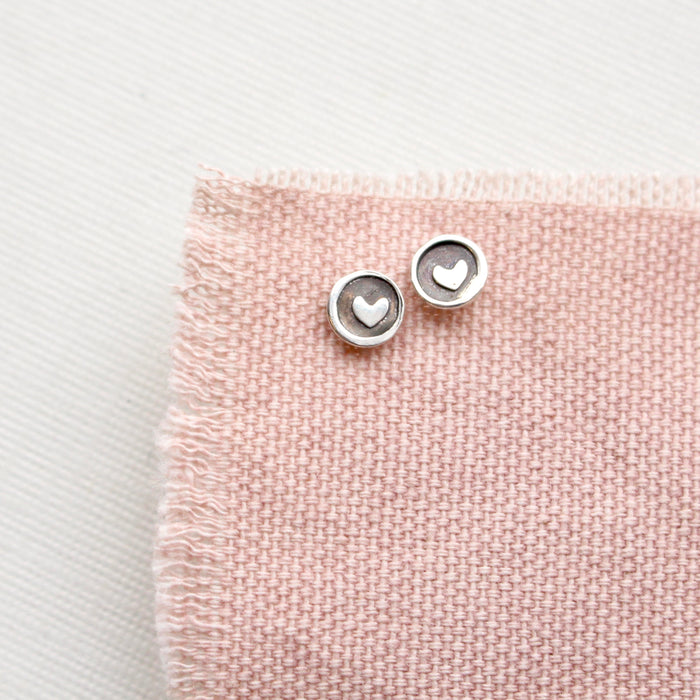 The teeny tiny heart post earrings styled on pink linen