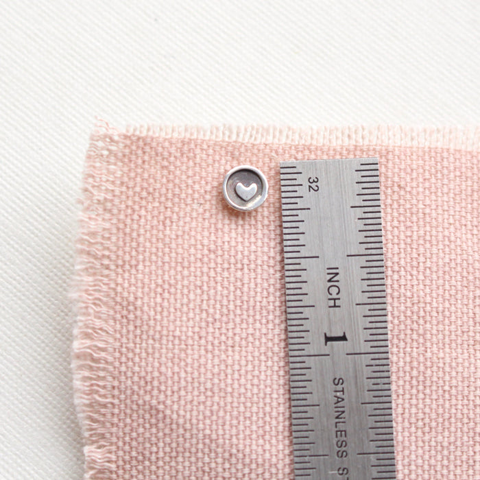 A teeny tiny heart post earring next to a ruler for size reference